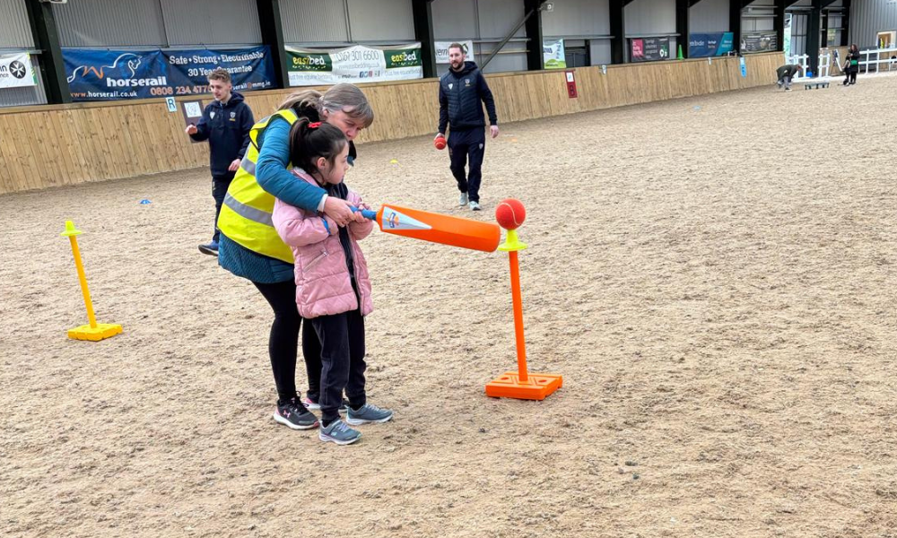 An activity day for young people, where a young girl is having a go at playing cricket. 