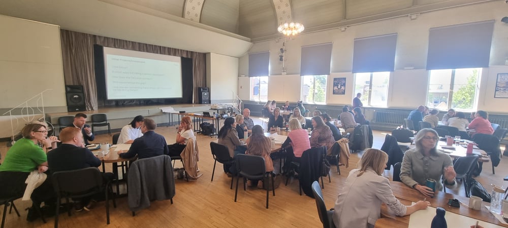 A photo showing people sat around 5 large tables inside The Anstice Hall in Madeley for System Leadership Training. The people are from various local organisations and are deep in discussions.